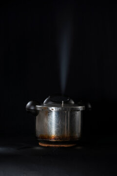 Close-up of a pressure cooker releasing steam through the lid, against a black background