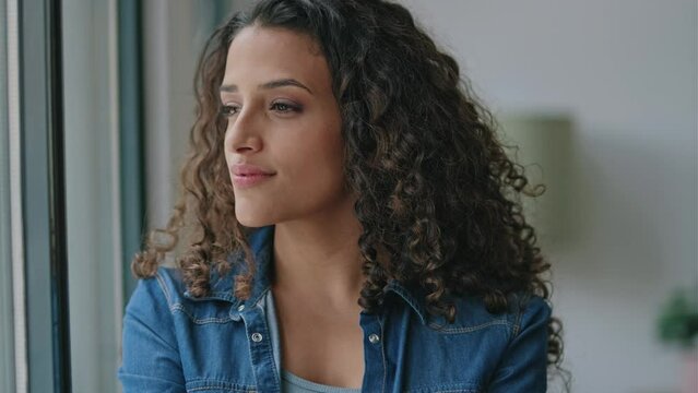 Video of beautiful young woman thinking while looking forward standing next to the window at home.