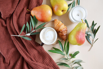 Cup of coffee with croissant, pears, candle, green branches on the light brown background. Fall season coffee. 