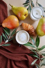 Cup of coffee with croissant, pears, candle, green branches on the light brown background. Fall season coffee. 