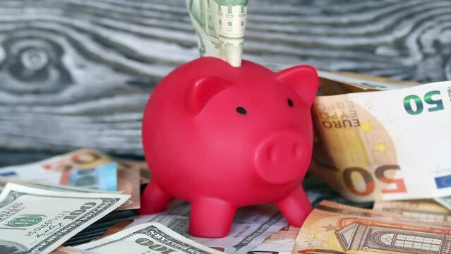 Piggy bank among dollar and euro banknotes. Money sticks out of her. Multicurrency savings. Difficulties in saving money.