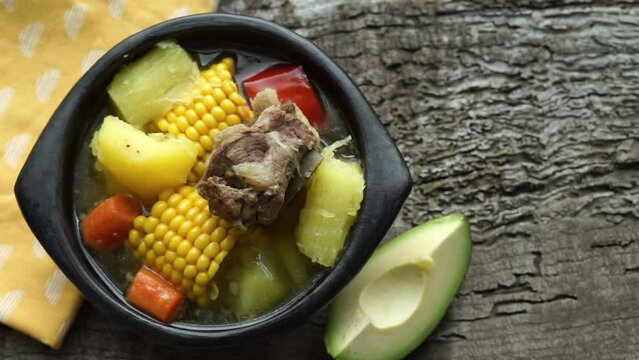Sancocho dish on a wooden base. Hand placing avocado and spices.