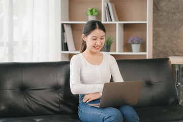 Fototapeta premium Asian woman happy holding laptop phone sitting sofa smiling good mood indoors indoors