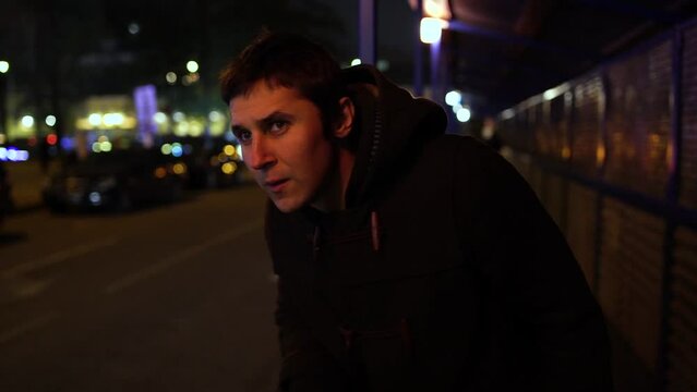Suspicious young man who looks like a criminal is following someone on the night street.