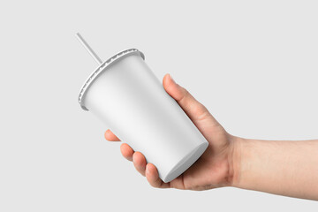 Paper soda cup in a hand with straw mockup template, isolated on light grey background. High resolution.