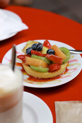 Shortbread tartlet with fruit in jelly on the red table. Blueberries, strawberries, peaches, kiwi