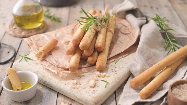 Traditional italian breadsticks grissini with rosemary, olive oil and sesame seeds on wooden countertop.
