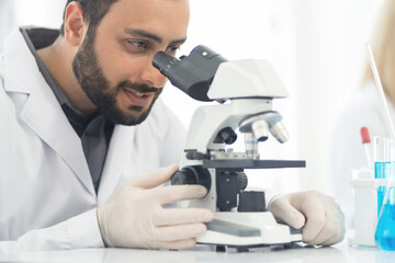 Man scientist looking through microscope doing analysis for germs and bacteria of test sample in the laboratory. Male specialist working with biotechnology research with microscope