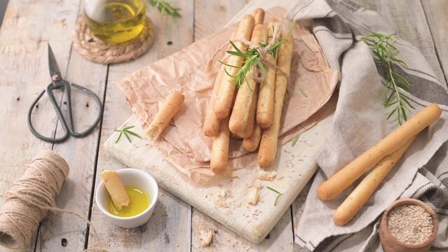 Traditional italian breadsticks grissini with rosemary, olive oil and sesame seeds on wooden countertop.