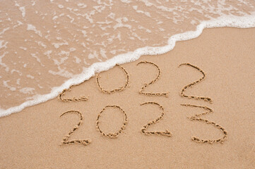 Inscription 2022 and 2023 numbers written on sand.  New Year 2023 replace 2022. Concept on the sea beach