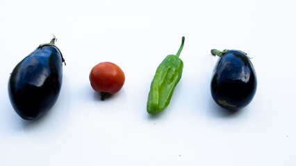 group of two organic aubergines, a tomato and a pepper from the garden on a white surface