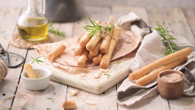 Traditional italian breadsticks grissini with rosemary, olive oil and sesame seeds on wooden countertop.