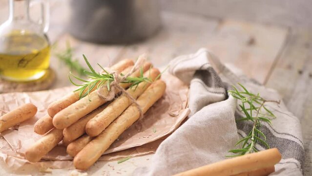 Traditional italian breadsticks grissini with rosemary, olive oil and sesame seeds on wooden countertop.