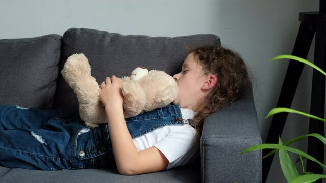 Cute little preteen girl sleep dream nap on cozy couch lying in comfortable pose with closed eyes. Tired tween child kid asleep with bear toy on sofa in silent light living room after active day