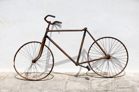 Old, rusty, superannuated bicycle wreck stands next to a pure white wall outdoor. 