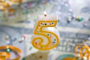 A 5 year celebration candle on U.S. currency.