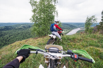 motorcycle handlebar view on biker standing on the edge of mountain, off-road dirt moto trip