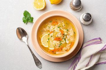 Italian lemon chicken orzo soup in bowl on concrete background