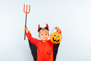 Happy Halloween! Cute little boy in devil halloween costume with trident and pumpkin basket...