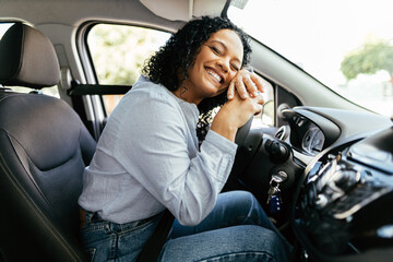 Young and cheerful woman enjoying new car hugging steering wheel sitting inside. Woman driving a...