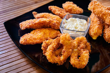 Breaded chicken fillet and king prawns with creamy sauce on a black plate