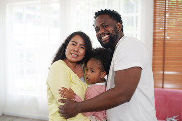 Shot of happy interracial family of mother father and their daughter inside modern apartment.
