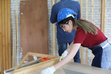 Side view portrait of modern female carpenter measuring wooden part making furniture over working table in workshop