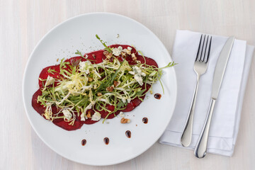 Beetroot carpaccio with arugula, dor blue, walnuts and salad on a plate.