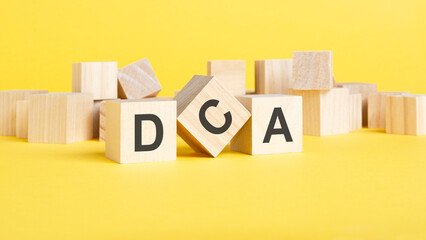 wooden blocks with word dca on yellow background. dollar cost averaging concept