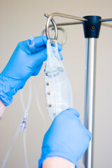 Gloved hands hang an IV bag for use with a patient.