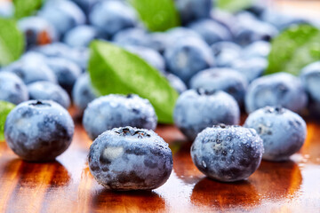 Close-up of a blueberry with green leaves and water drops on a wooden background