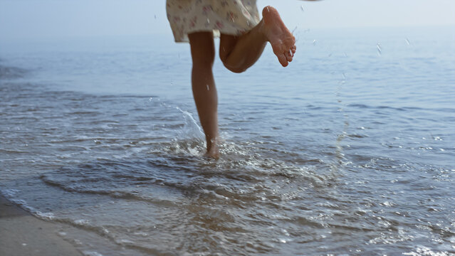 Bare Woman Legs Jumping On Sea Waves Close Up. Girl Feet Splashing In Water.