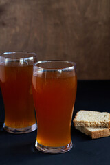 glass of beer and sandwich on the wooden table. two high Glasses of fresh kvass with bread on black background with copy space. vertical