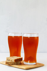 summer iced drinks. glass of beer and sandwich on the cutting board. two high Glasses of fresh kvass with bread on white background with copy space. vertical