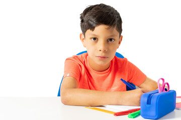 Boy writing in his notebook on the white desk table with several colored pencils and the pencil case. Back to school. High quality photo