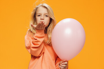 a cute, beautiful school-age girl stands on a bright background with a balloon and sends an air kiss to the camera. Horizontal photo with empty space for advertising layout
