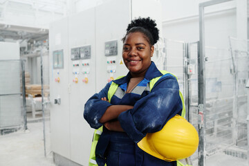 Young successful black woman in uniform holding safety helmet in hand while keeping her arms...
