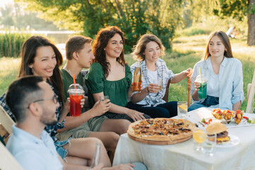 Group of friends are relaxing together outdoor. Young cheerful people clink glasses and laugh.