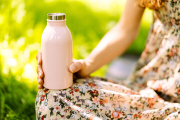 Close-up of steel eco thermo water bottle in female hand. Green background in the park. Copy space concept. Space for text. Plastic free. Zero waste concept. Selective focus. 