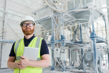 Young confident engineer or technician of modern production factory in workwear, eyeglasses and protective helmet looking at camera