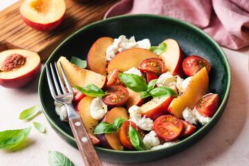 Healthy summer fruit and cheese salad with peach, mozzarella, cherry tomatoes and basil
