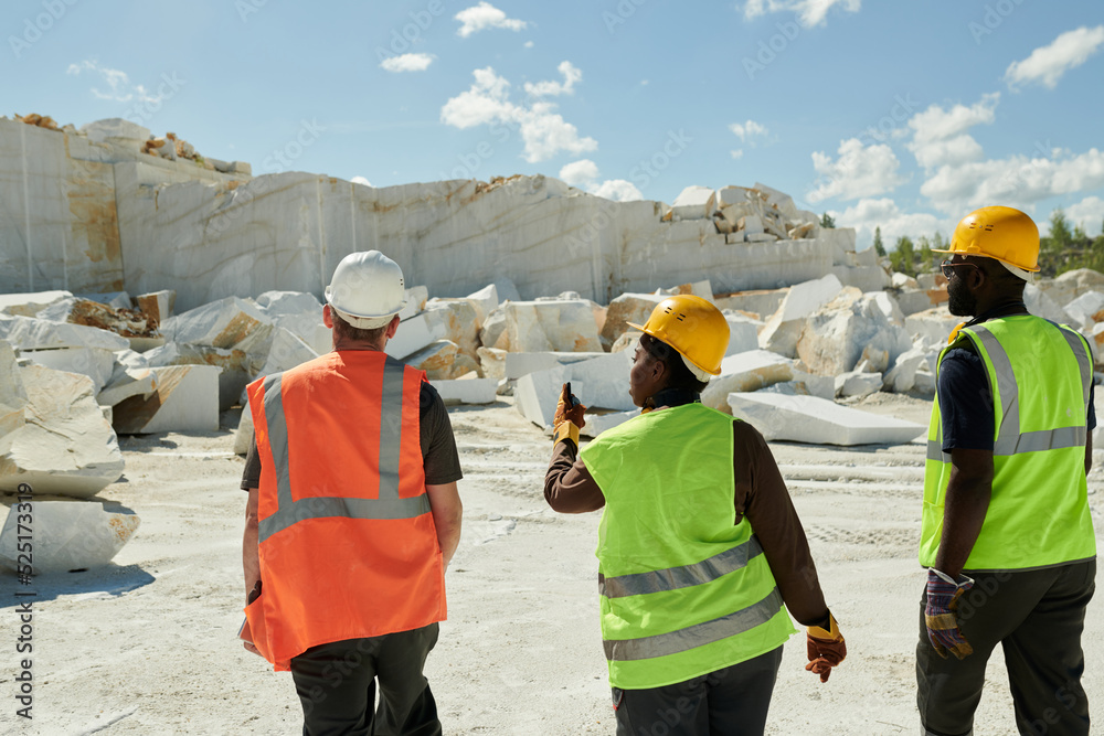Poster rear view of several young intercultural workers of marble quarry moving towards white rocks and dis