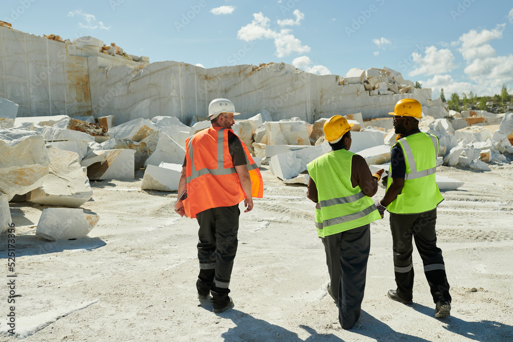 Aufkleber back view of three multicultural workers of marble quarry in workwear and safety helmets moving down