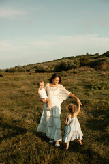 a mother with her son and daughter in light clothes are walking on the meadow