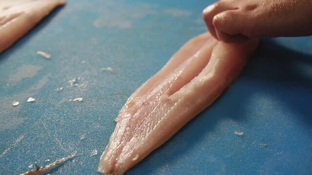 Chef fillets codfish on cutting board with a knife.