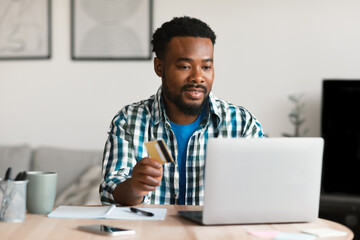 African American Male Using Laptop And Credit Card Shopping Indoors