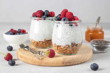Superfoods concept : chia pudding with homemade granola, fresh berries and honey on light gray table. Healthy eating