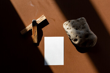 Still life scene with hard shadows on brown background in sunlight palo Santo and blank business,...