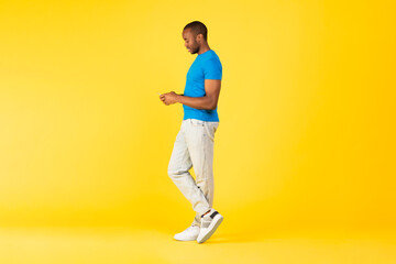 Fototapeta na wymiar Black Male Using Cellphone Texting Standing Over Yellow Studio Background