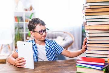 Portrait of student with a tablet computer. boy child sits at table with stacks of books pushing...